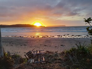 A beach with a sunset, a wooden bench, and some vegetation.
