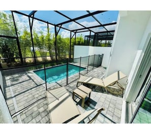 A modern outdoor pool area with a glass enclosure, a pool, and lounge chairs. - The Sun-Kissed Retreat / near Disney (Davenport)