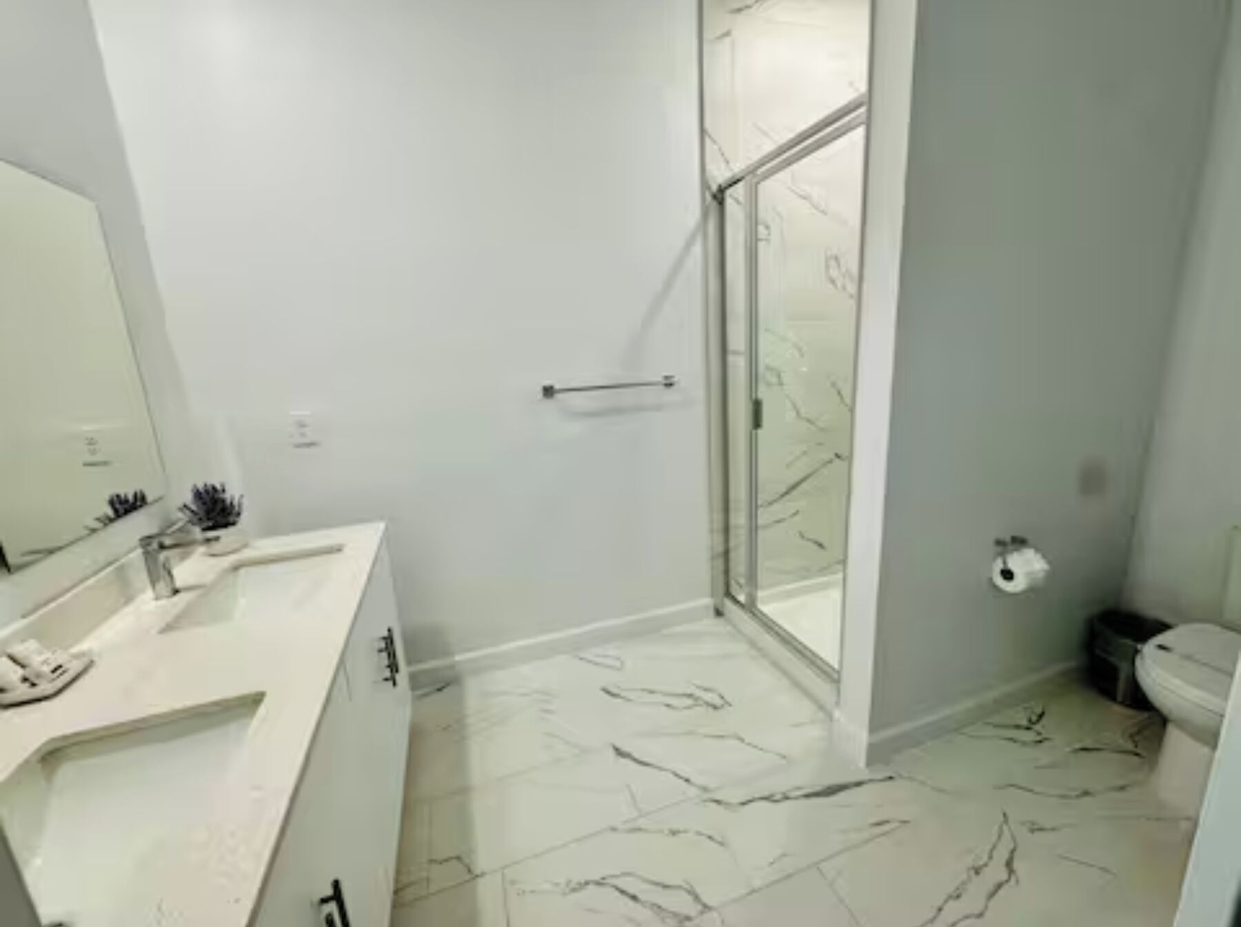 Une salle de bain avec un sol en marbre blanc, une douche en verre, un lavabo blanc et des toilettes.