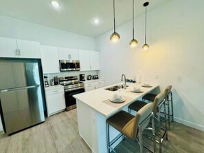 A modern kitchen with white cabinetry, stainless steel appliances, and a central island with bar stools.