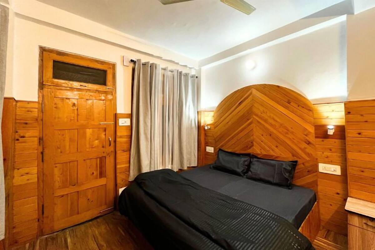 Quarto com painéis de madeira, uma cama, uma porta e uma cortina.