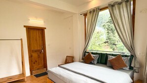 Un dormitori amb un llit de fusta, una finestra amb cortines, un banc amb tapisseria verda i una porta de fusta.