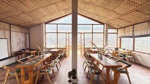 Una habitació espaiosa amb taules i cadires de fusta, grans finestres i un sostre alt amb un disseny trenat.