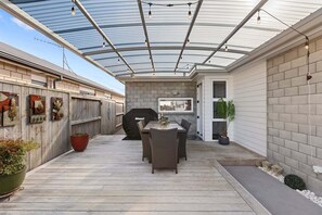 Un patio cubierto con una mesa, sillas, una parrilla y plantas en macetas.