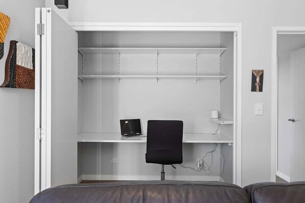 Una habitación pequeña con escritorio integrado, una silla y una computadora port átil.