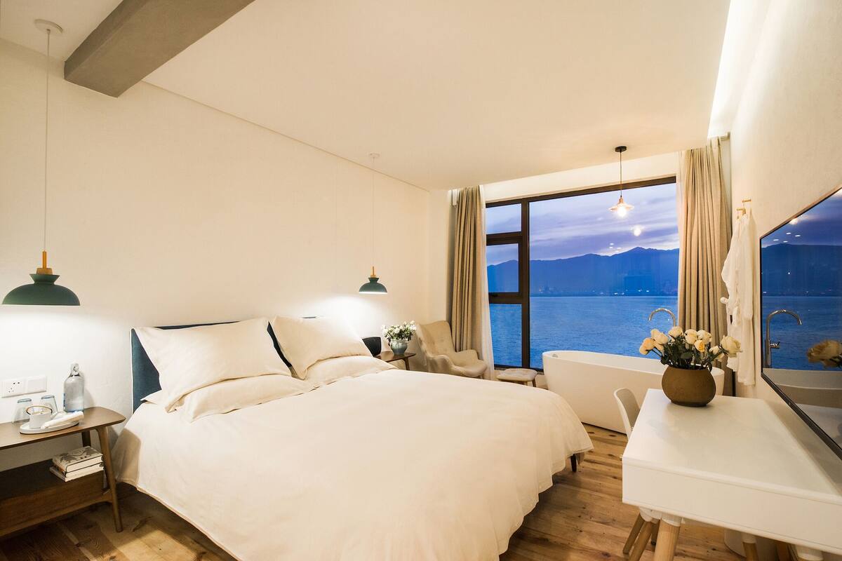 A hotel room with a large bed, a desk, a chair, and a view of the sea.