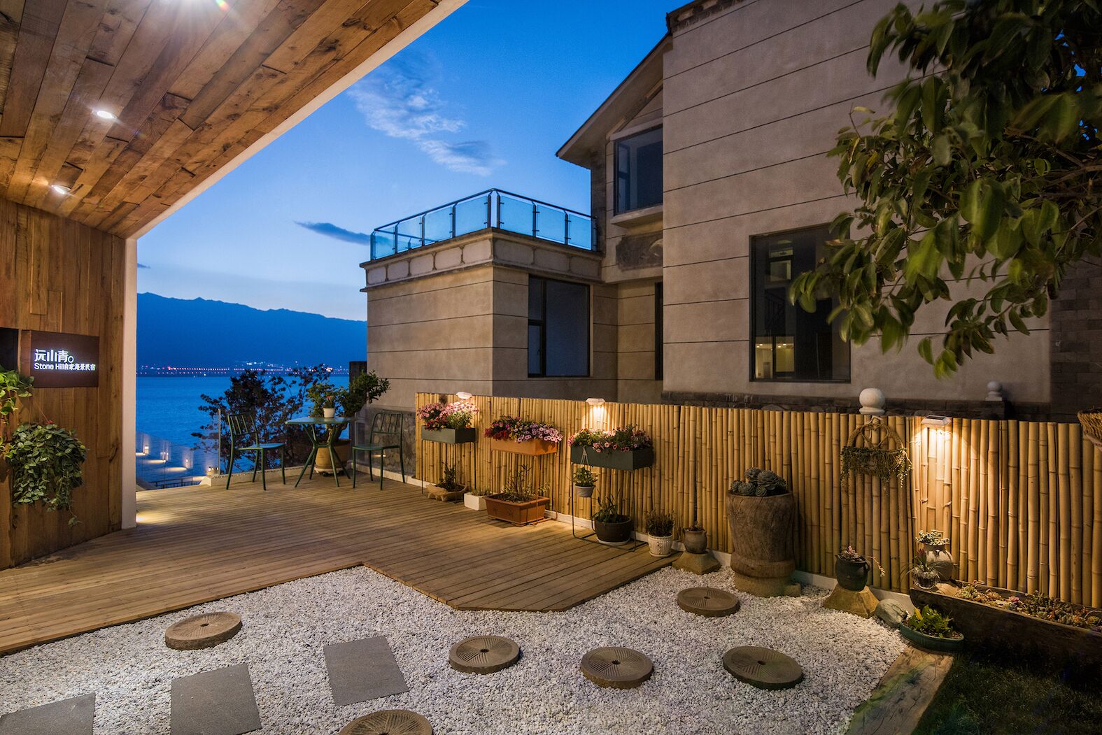 A modern outdoor patio with a wooden deck, potted plants, and a view of the sea.