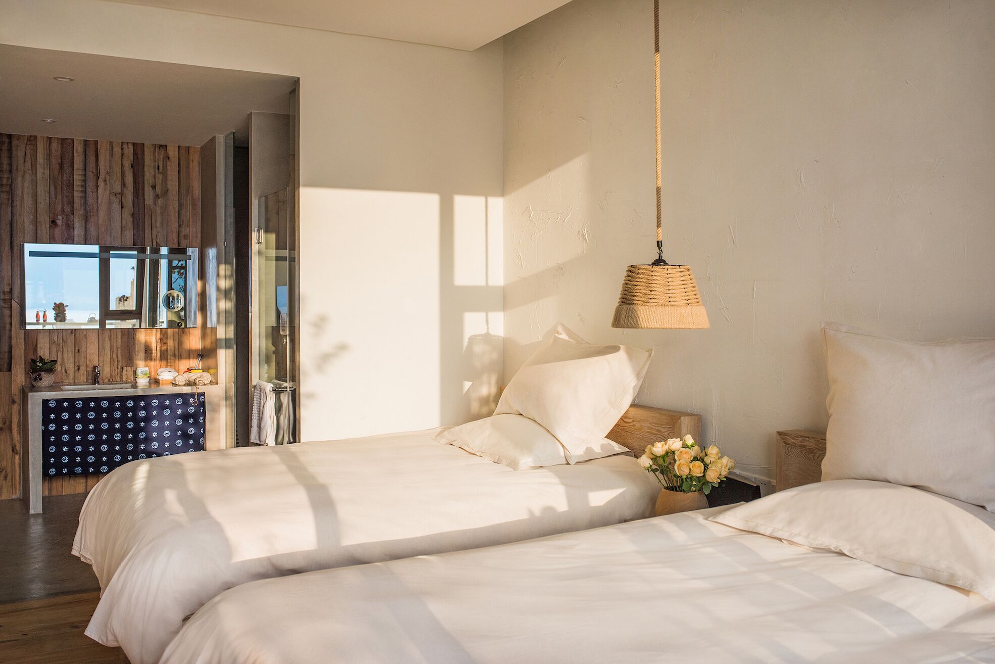 A bedroom with two beds, a hanging light fixture, and a view of the bathroom.