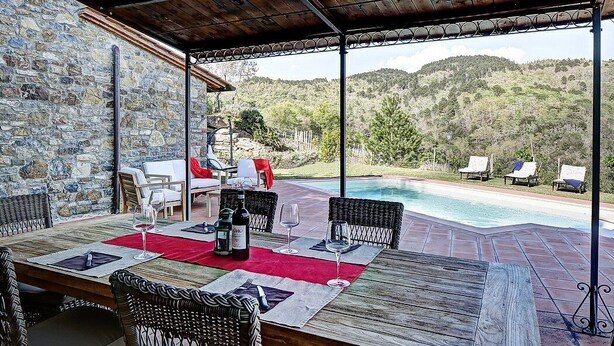 Un área de comedor al aire libre con muros de piedra, una piscina y sillas de descanso.
