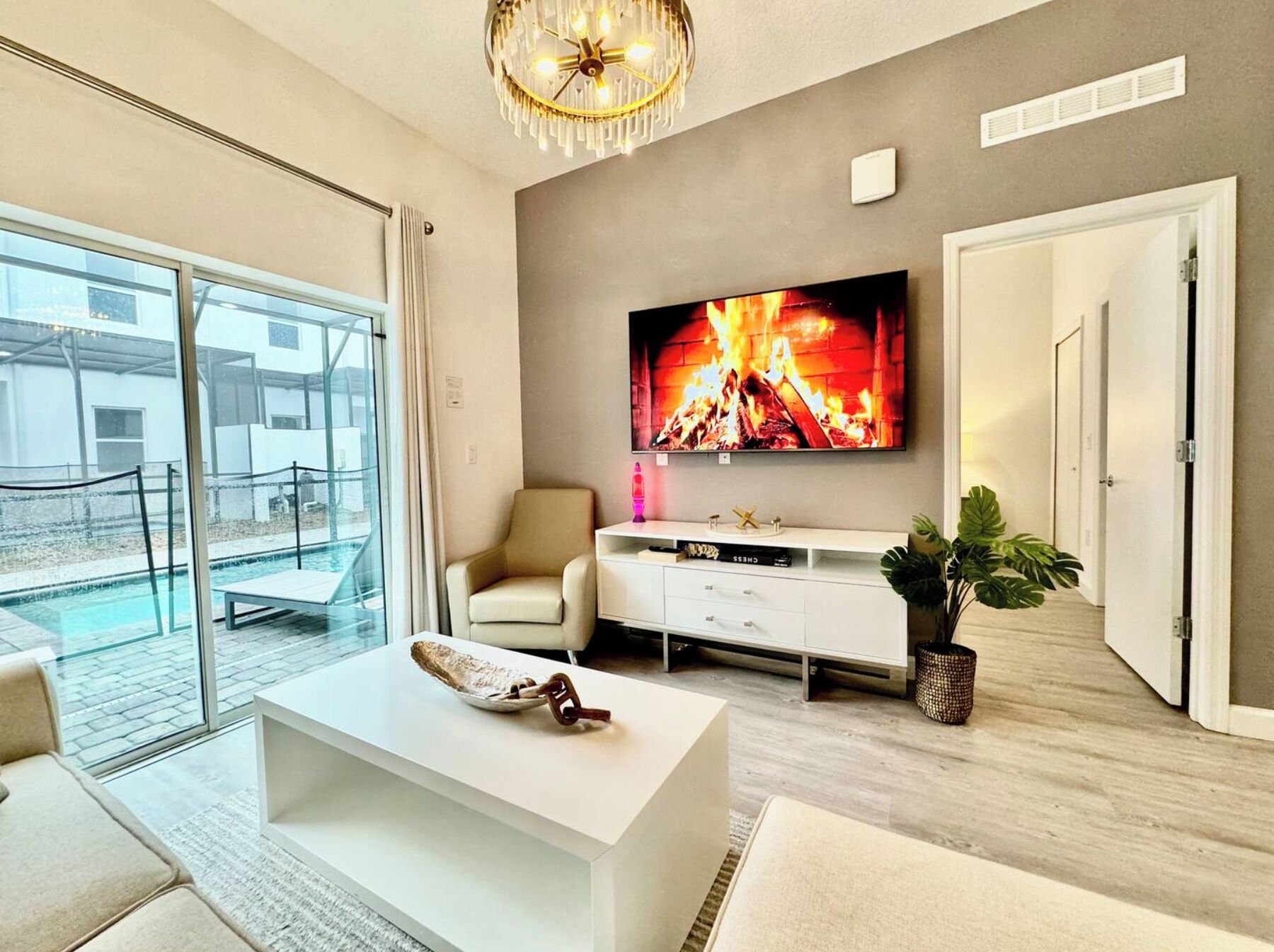 A modern living room with a large TV, a white sofa, a coffee table, and a plant.