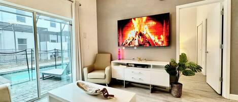 A modern living room with a large TV, a white sofa, a coffee table, and a plant.