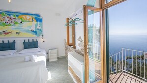 Ein Schlafzimmer mit großem Fenster mit Meerblick, einem Gemälde einer Küstenszene und einem Balkon mit Blick aufs Meer.