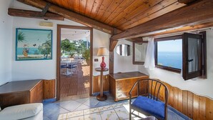 Ein gemütliches Zimmer mit Holzbalken, einem Holzkasten, einem Stuhl, einem Tisch und Meerblick durch ein Fenster.