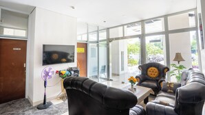 A modern waiting area with leather sofas, a flat-screen TV, and large windows offering a view of the outdoors. - Tamastu Blue Sapphire Apartel Cakung (Jakarta)