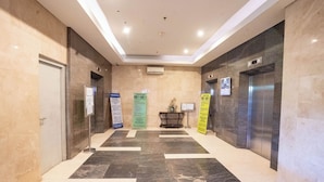 A modern hotel lobby with a marble floor, two elevators, and informational signs on the walls. - Tamastu Blue Sapphire Apartel Cakung (Jakarta)