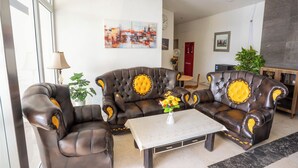 A living room with two brown leather sofas with yellow accents, a white coffee table, and a potted plant. - Tamastu Blue Sapphire Apartel Cakung (Jakarta)