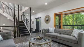 A modern living room with a staircase, a grey sofa, and a round coffee table. - Ultimate Treehouse Mansion w/ Swim Spa, Sleeps 31 (Lakewood)