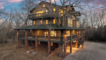 A multi-story log cabin with a balcony, surrounded by trees.