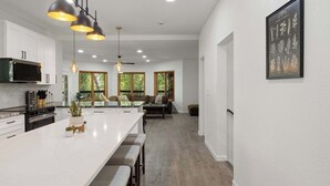 A spacious kitchen with a large island, pendant lighting, and a dining area with a view of trees. - Ultimate Treehouse Mansion w/ Swim Spa, Sleeps 31 (Lakewood)