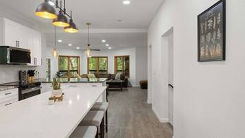 A spacious kitchen with a large island, pendant lighting, and a dining area with a view of trees.