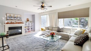 Uma sala de estar moderna com lareira, uma mesa de centro de vidro, um sofá e um ventilador de teto.