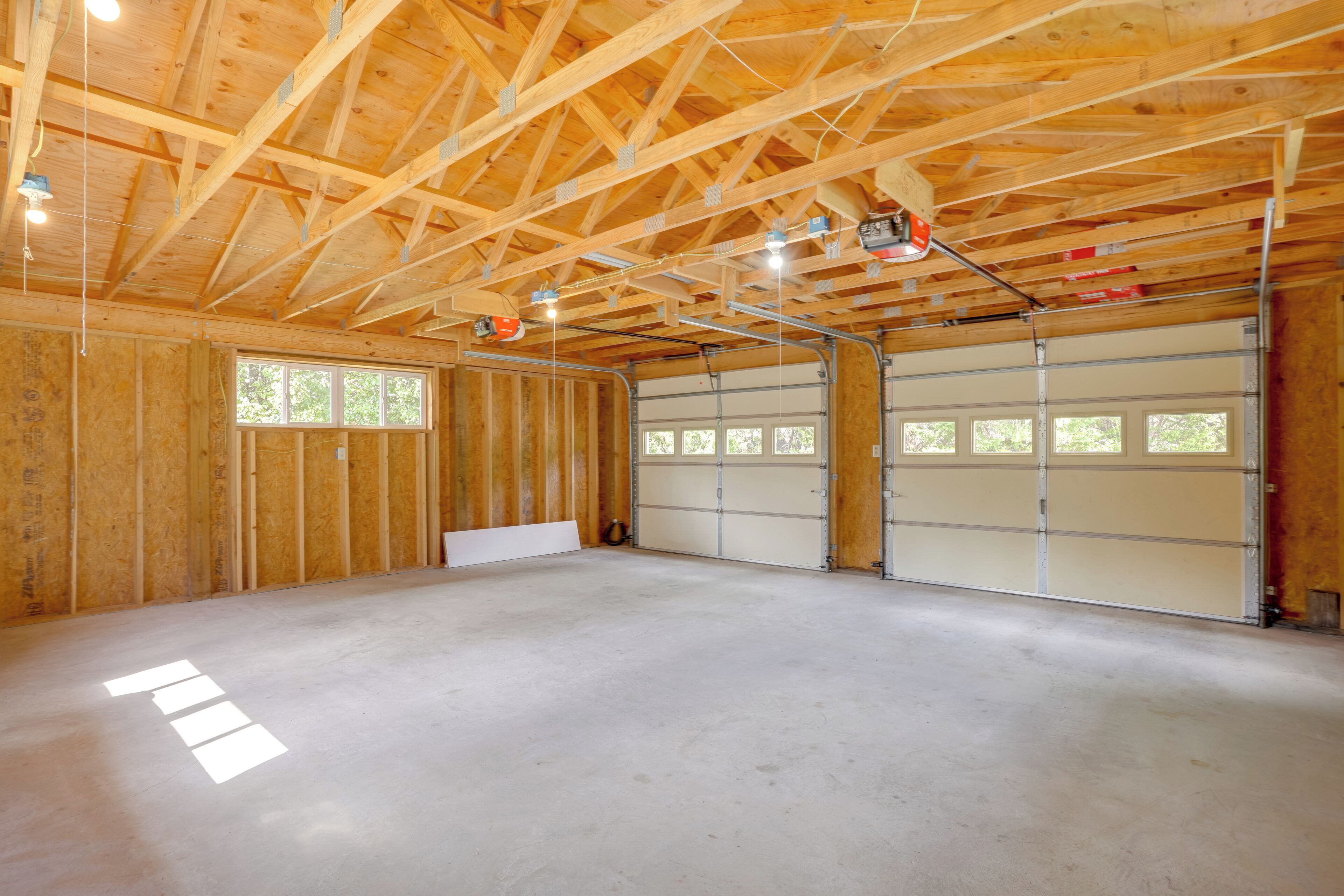 Un grand garage doté d’un sol en béton, de murs en bois et d’un plafond haut avec des poutres apparentes.