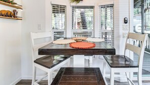 Un comedor con una mesa de madera oscura, sillas blancas y un adorno de piña en la pared.