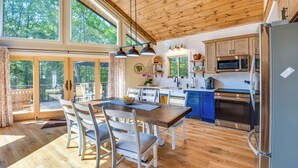 A spacious kitchen with wooden flooring, a dining area with white chairs, and a large window overlooking greenery. - Secluded Lake Lanier Cabin w/ Game Area (Gainesville)
