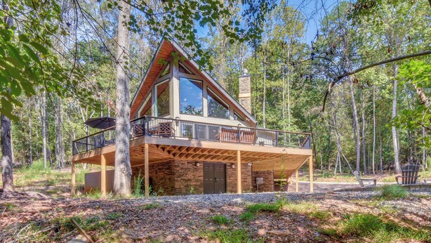 A modern cabin with a large glass window, a balcony, and a stone chimney. - Secluded Lake Lanier Cabin w/ Game Area (Gainesville)