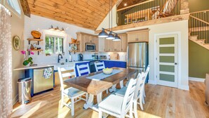 A spacious kitchen with wooden cabinets, a dining area with white chairs, and a wooden ceiling. - Secluded Lake Lanier Cabin w/ Game Area (Gainesville)