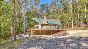 A two-story cabin with a stone chimney, a covered porch, and a gravel driveway. - Secluded Lake Lanier Cabin w/ Game Area (Gainesville)