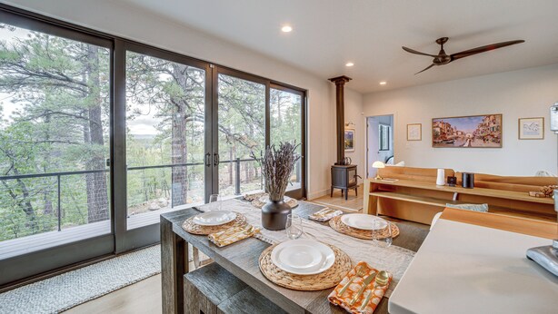 A dining area with a large window, a ceiling fan, and a view of trees. - Modern Cabin Living! Mtn-View Gem in Munds Park (Munds Park)