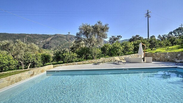 A rectangular swimming pool with clear blue water, surrounded by a stone wall and a grassy area with trees and a hill in the background. - Villa Pascal C: A characteristic and welcoming apartment that is part of a villa surrounded by meadows and by green hills, with Free WI-FI. (Mirto)