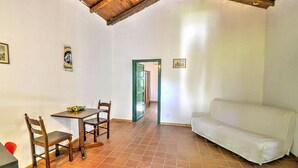 A room with a tiled floor, a white sofa, a wooden table with chairs, and a door leading to another room. - Villa Pascal C: A characteristic and welcoming apartment that is part of a villa surrounded by meadows and by green hills, with Free WI-FI. (Mirto)
