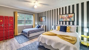 Une chambre d’hôtel avec deux lits, un ventilateur de plafond, une fenêtre avec des rideaux, un tableau et une armoire rouge.
