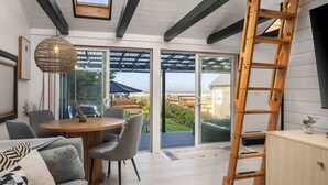 A modern interior with a dining area, large sliding glass doors to a deck, and a wooden ladder.