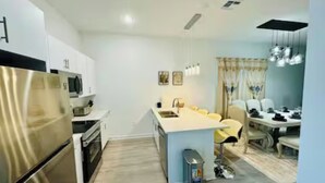 A modern kitchen with stainless steel appliances, a central island, and a dining area with a table and chairs. - The Villa Retreat / near Disney (Davenport)