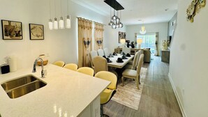 A modern kitchen with a central island, a dining area with yellow chairs, and a living space with a sofa and TV. - The Villa Retreat / near Disney (Davenport)