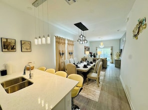 Eine moderne Küche mit Kochinsel, ein Essbereich mit gelben Stühlen und ein Wohnbereich mit Sofa und Fernseher.