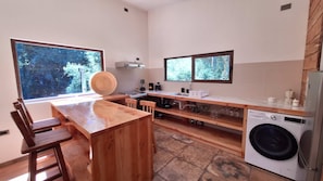 Una cocina moderna con una mesa de madera, sillas, una lavadora y un ventanal con vistas a árboles.