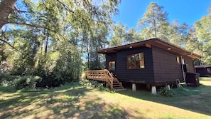 Eine Holzhütte mit einer Holzterrasse, umgeben von dichtem Wald.