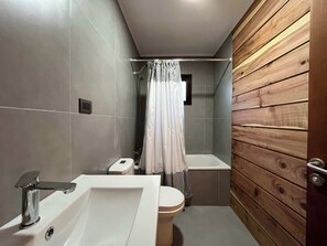 A bathroom with a toilet, sink, shower, and wooden paneling.