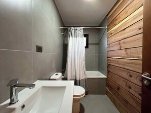 Ein Badezimmer mit Toilette, Waschbecken, Dusche und Holzwandverkleidung.