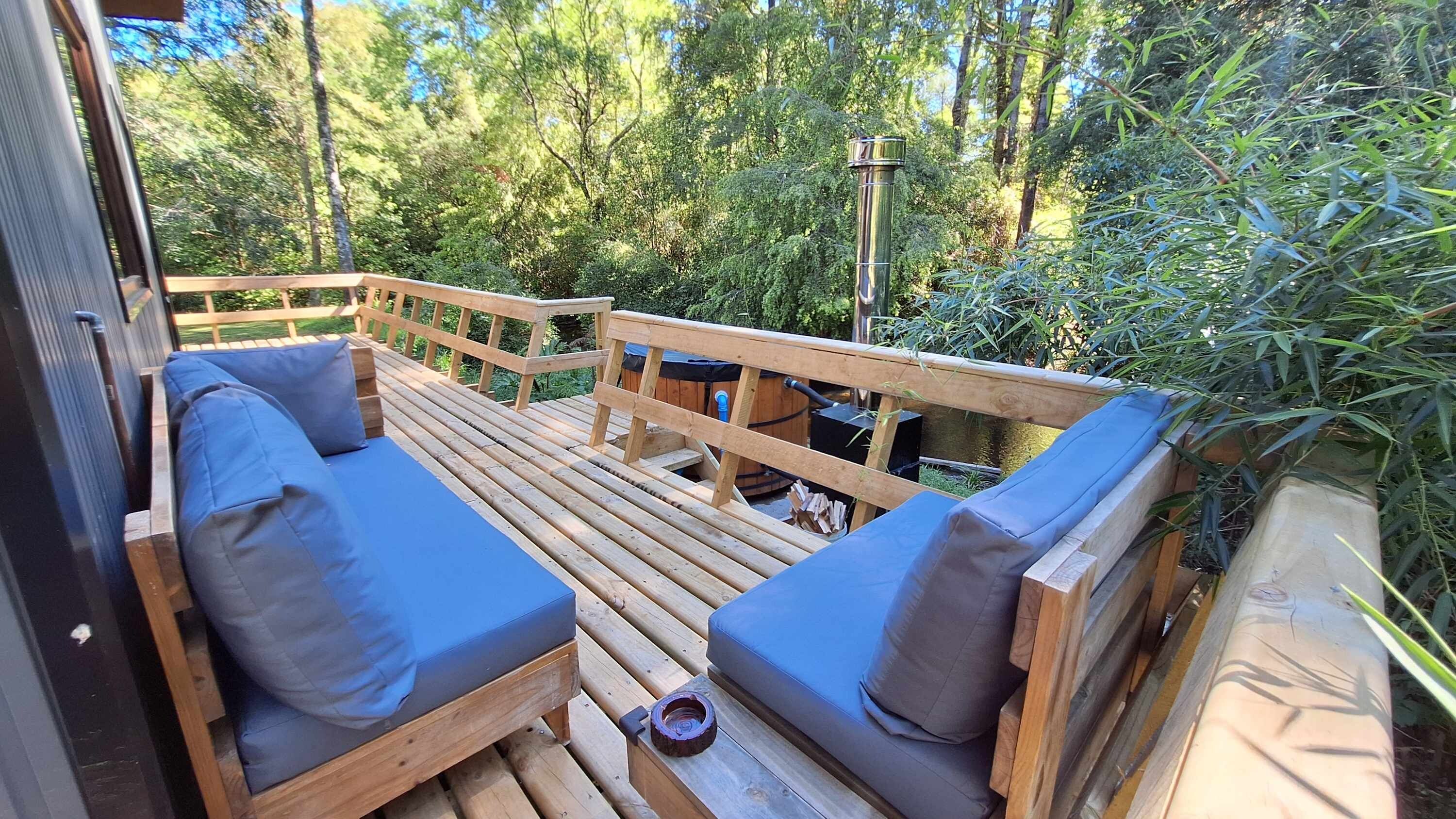 An outdoor deck with wooden furniture and a view of a forest.