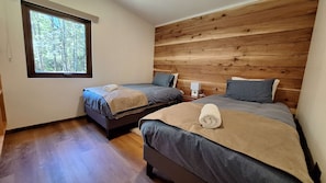 Habitación con dos camas, cabecero de madera, una ventana y una mesita de noche con lámpara.