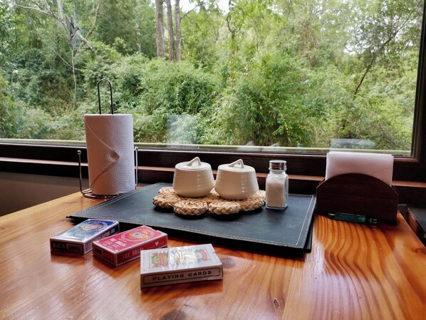 A wooden table with a black placemat, a tissue roll, a salt shaker, a sugar container, and playing cards.