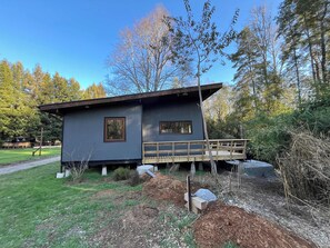 A single-story cabin with a wooden deck, surrounded by a natural landscape.