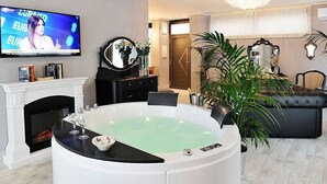 A living room with a large TV, a fireplace, a round hot tub, a sofa, and a potted plant. - Villa Bacio: An elegant and welcoming two-story villa situated at a short distance from the Adige river, with Free WI-FI. (Castelbaldo)