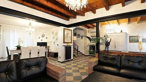 A spacious living room with a fireplace, a dining area with a table and chairs, and a black leather sofa. - Villa Bacio: An elegant and welcoming two-story villa situated at a short distance from the Adige river, with Free WI-FI. (Castelbaldo)