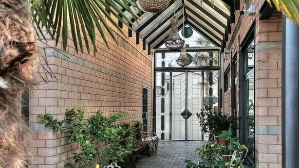 A covered walkway with brick walls, potted plants, and a large glass door at the end. - Villa Bacio: An elegant and welcoming two-story villa situated at a short distance from the Adige river, with Free WI-FI. (Castelbaldo)